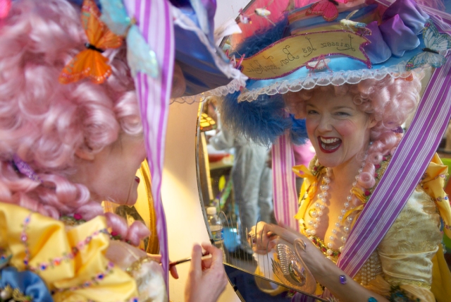Woman dressed as Marie Antoinette laughs while looking into a mirror on Mardi Gras day.